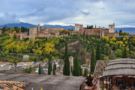 Image taken from the Saint Nicholas viewpoint of the Alhambra landscape on a cloudy autumn day, the forest with green and yellow leaf trees and houses of the AlbaicÃ­nの写真素材