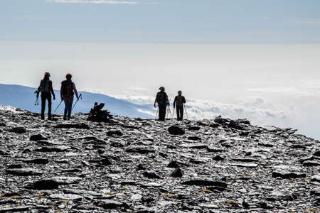silhouettes of hikers coming down from the top of Mulhacen with a sea of low clouds in the backgroundの写真素材