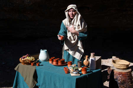 Motril, Granada, Spain, December 23, 2018: Recreation of a Christmas Nativity Scene in the annex of Motril de Tablones. Woman offering wine with small ceramic glasses and bunches of grapesのeditorial素材