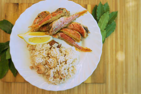 Fried rice  and small fish in plate on table. Bay leaves and lemon. Outdoors Food.   の写真素材