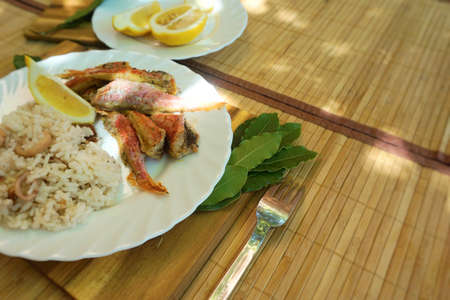 Fried rice  and small fish in plate on table. Bay leaves and lemon. Outdoors Food.   の写真素材