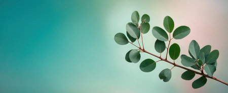 A slender branch with vibrant green leaves is set against a beautiful teal and pink backdrop. High quality photoの素材