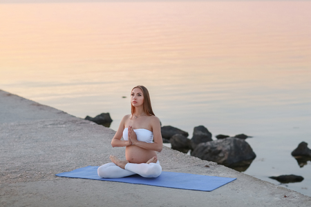 Beautiful pregnant woman doing yoga at the seasideの写真素材