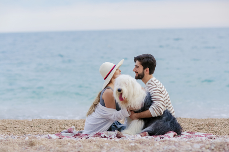 Alternative family with one lady a man and a dog together at the beach enjoying a picnic in friendship and partenership. Having fun in outdoor leisure activity together with love for animalの写真素材