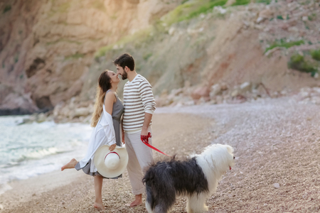 Happy young couple walking with big dog on the beach in summerの写真素材