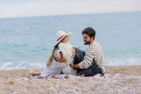 Alternative family with one lady a man and a dog together at the beach enjoying a picnic in friendship and partenership. Having fun in outdoor leisure activity together with love for animalの写真素材