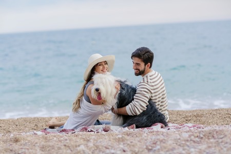 Alternative family with one lady a man and a dog together at the beach enjoying a picnic in friendship and partenership. Having fun in outdoor leisure activity together with love for animalの写真素材