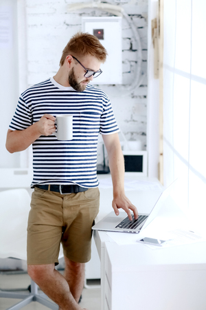 Successful businessman. Office worker. Portrait of bearded businessman. Serious businessman. Man standing at table and holds laptop. Handsome bearded office worker.の写真素材