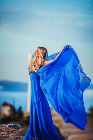 Sensual woman stand on the stone of peak mountain. blond woman with long hair walk on cliffs edge and looking down on forest and mountain background. blondy girl enjoy wind. windy weatherの写真素材