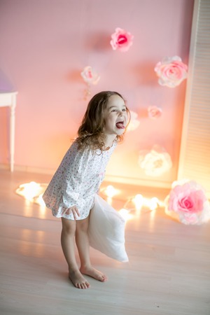 Little beautiful girl with light pillows in a cozy room.の写真素材