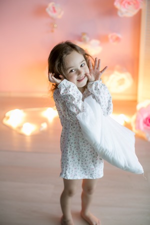 Little beautiful girl with light pillows in a cozy room.の写真素材