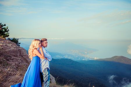 Beautiful couple of newlywed hugging at wedding day on cliff with ocean view. Stylish bride and elegant groom look at each other with love. Concept honeymoon, family, marriage, just marriedの写真素材