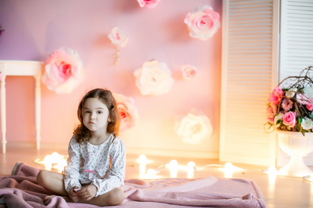 A little girl in a homely atmosphere against a wall with glowing lights.の写真素材