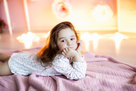 A little girl in a homely atmosphere against a wall with glowing lights.の写真素材