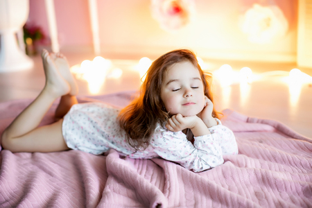 A little girl in a homely atmosphere against a wall with glowing lights.の写真素材