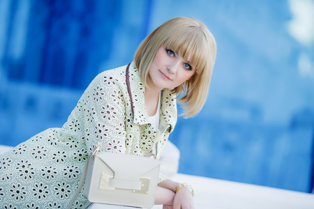 Autumn fashionable image of cute young woman with short hairs and candid smile. Trendy coat, denim jeans. Student female posing inver yellow wall. Outdoor .の写真素材