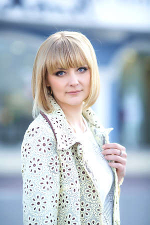 Autumn fashionable image of cute young woman with short hairs and candid smile. Trendy coat, denim jeans. Student female posing inver yellow wall. Outdoor .の写真素材