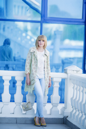 Autumn fashionable image of cute young woman with short hairs and candid smile. Trendy coat, denim jeans. Student female posing inver yellow wall. Outdoor .の写真素材