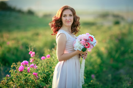 A bride in a white dress holds a bouquet of roses and callas on the background of green grassの写真素材