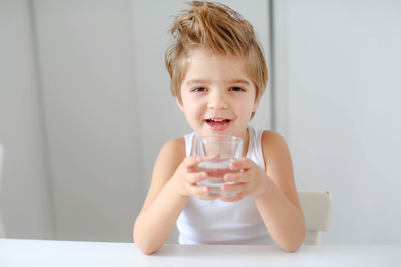 Cute smiling boy with glass of water isolated on a white background.の写真素材