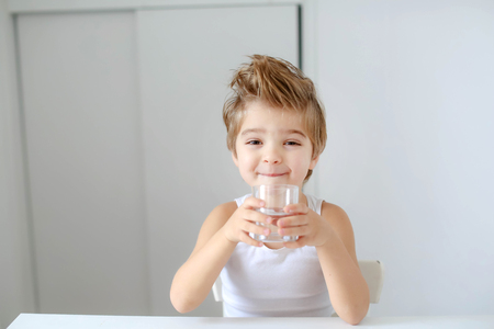 Cute smiling boy with glass of water isolated on a white background.の写真素材