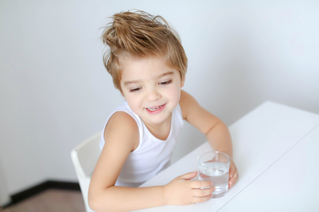 Cute smiling boy with glass of water isolated on a white background.の写真素材