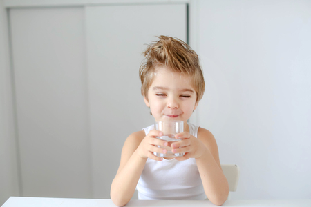 Cute smiling boy with glass of water isolated on a white background.の写真素材