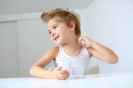 Cute smiling boy with glass of water isolated on a white background.の写真素材