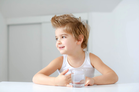 Cute smiling boy with glass of water isolated on a white background.の写真素材