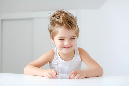 Cute smiling boy with glass of water isolated on a white background.の写真素材