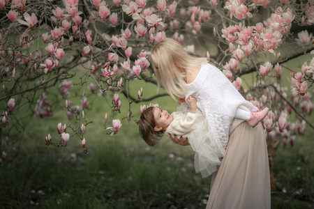 Portrait of happy joyful child in white clothes over tree flowers blossom background. Family playing together outside. Mom cheerfully hold little daughter Newborn spring concept.の写真素材