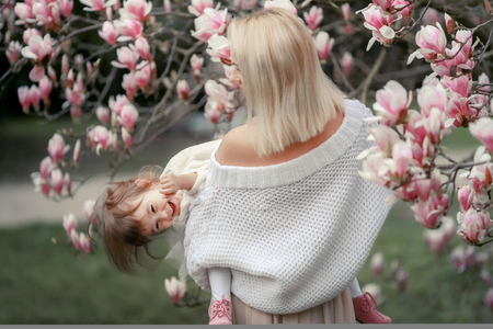 Portrait of happy joyful child in white clothes over tree flowers blossom background. Family playing together outside. Mom cheerfully hold little daughter Newborn spring concept.の写真素材