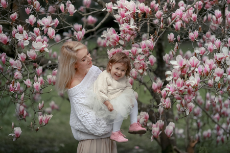 Portrait of happy joyful child in white clothes over tree flowers blossom background. Family playing together outside. Mom cheerfully hold little daughter Newborn spring concept.の写真素材