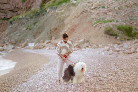 young caucasian male sitting with dog on beach during sunset or sunriseの写真素材