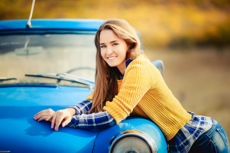 Smiling cheerful girl with long hair, wearing in black hat and yellow sweater, and enjoys freedom, standing next to road. Portrait of adorable young woman outside.の写真素材