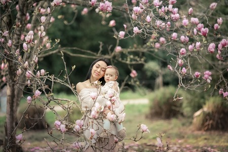 Young mother and little daughter in autumn park play with Japanse magnolia leaves. Happy weekend with family in autumnal forest park. People in park. Smiling woman and baby in outdoor. Fall. Sunny dayの写真素材