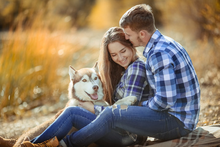 A young couple is sitting by the lake at sunset with a Husky breed dogの写真素材