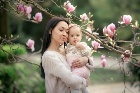 Young mother and little daughter in autumn park play with Japanse magnolia leaves. Happy weekend with family in autumnal forest park. People in park. Smiling woman and baby in outdoor. Fall. Sunny dayの写真素材