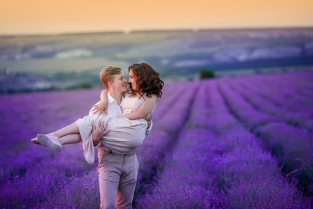 a loving couple standing in a lavender field looking at a pink cloud in the shape of a heart.の写真素材