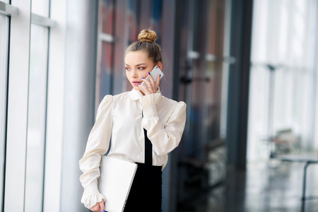A woman in a business suit with Long hair and red lips. Dressed in white blouse wiyh notepad in her handsの写真素材
