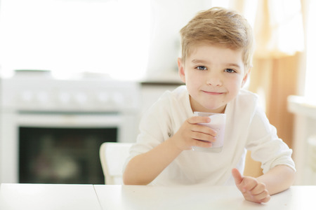 Kid or blonde happy boy eating at table. Childhood and happiness, independence. Breakfast, morning, family. Small boy child eat banana and drink milk. Healthy food and vitamin. dieting, vegetarian.の写真素材