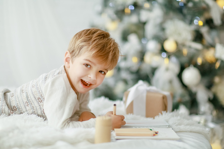 Beautiful little baby boy in pajamas with stars celebrates Christmas. New Years holidays. Toddler play in white Christmas sleigh in the festively decorated room, copy space on right area.の写真素材