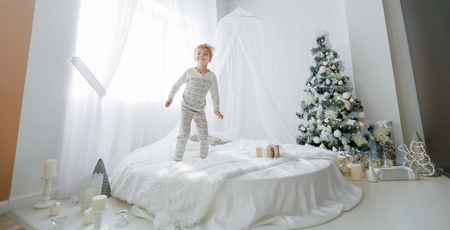 Beautiful little baby boy in pajamas with stars celebrates Christmas. New Years holidays. Toddler play in white Christmas sleigh in the festively decorated room, copy space on right area.の写真素材