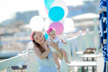 Happy mother and child with colorful balloons walking together on beach near sea.の写真素材