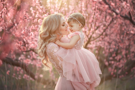 Portrait of young beautiful mother with her little girl. Close up still of loving family. Attractive woman holding her child in pink flowers and smiling.の写真素材