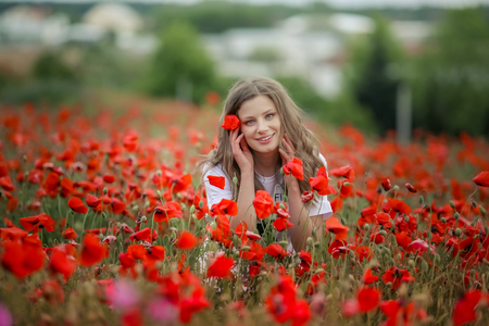 Beautiful happy smiling teen girl portrait with red flowers on enjoying in poppies field nature background. Makeup and curly hair style. Lifestyleの写真素材