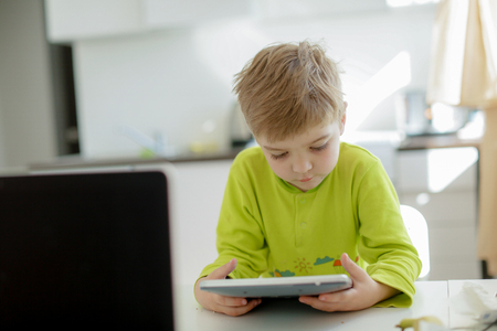 Boy playing on electronic gadget tablet in his bedroom. Social problem of communication of children in the modern worldの写真素材