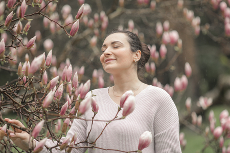 Spring Beautiful romantic red haired girl in white lace dress and jeans standing near blooming tree with transparent umbrellaの写真素材