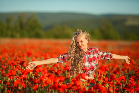 Young blonde in a red shirt in the poppy flower fieldの写真素材