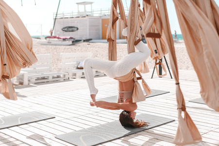 Beautiful woman engaged in antigravity yoga outdoors by the sea on the beach.の写真素材